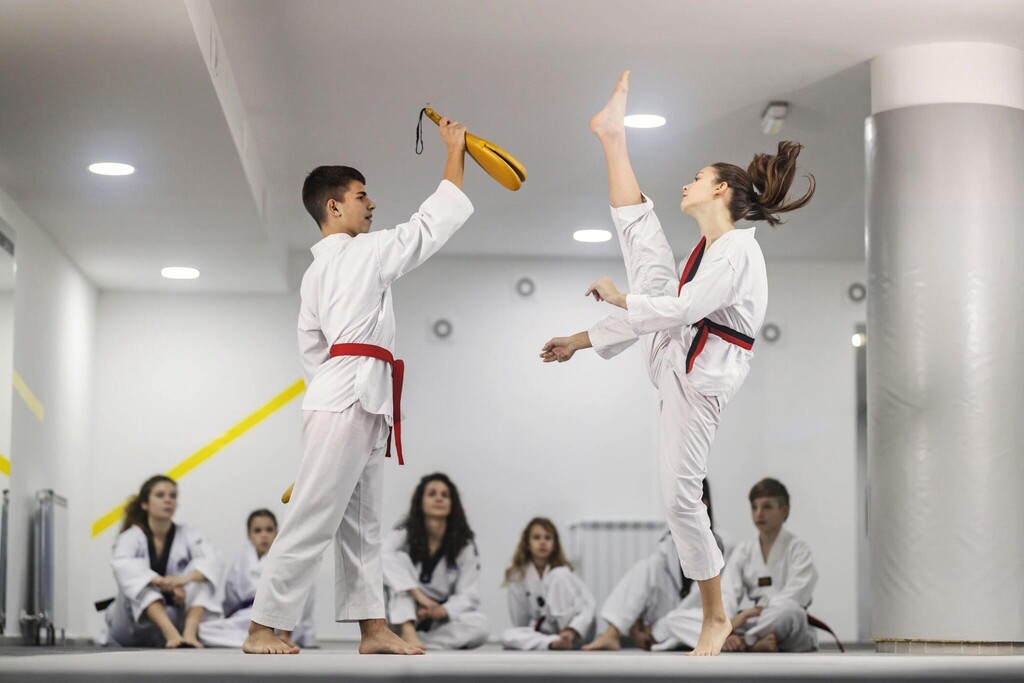Taekwondo girl is practicing attack on training and other teammates are sitting and watching.